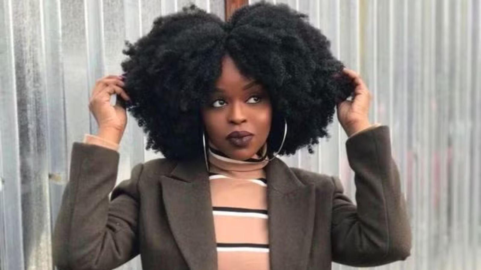 A beautiful black woman with dark skin, fluffing up her afro with a smile on his face.