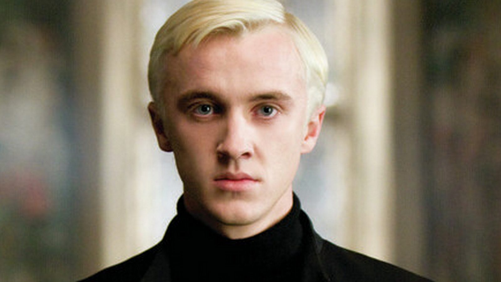 Draco Malfoy - a white young man with short neat platinum blonde hair in a black suit.