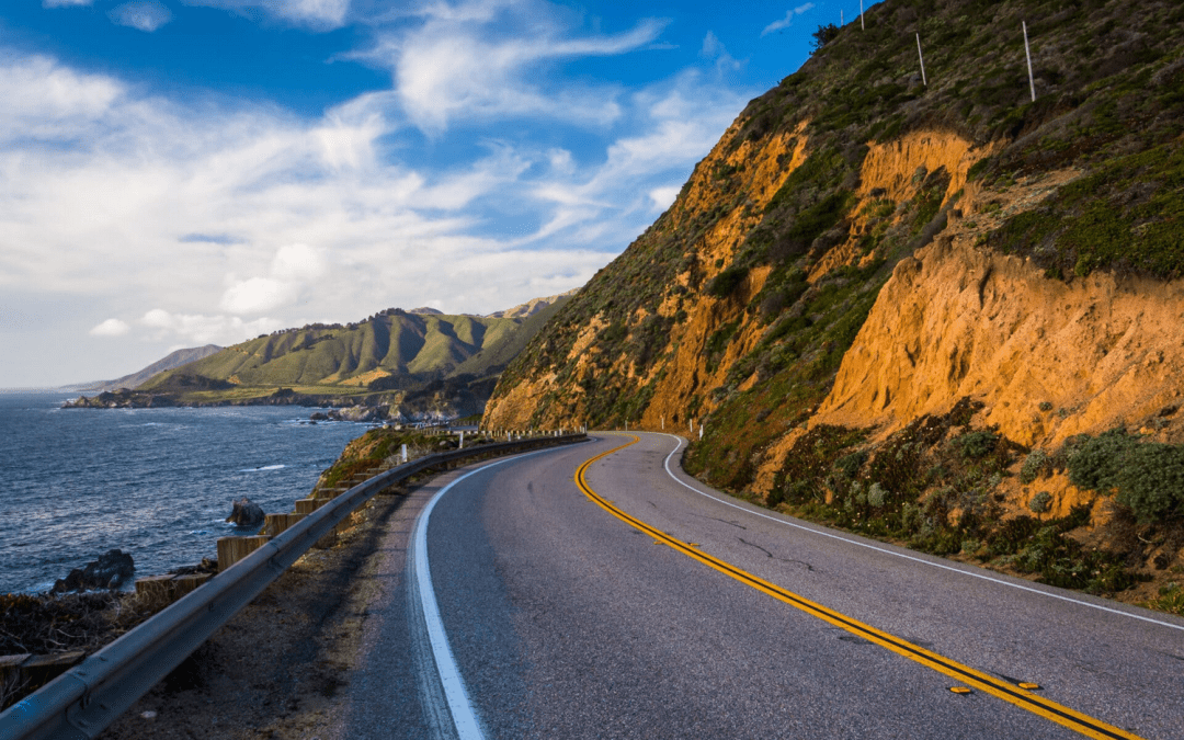 a photo of a coastal highway alongside a hill.