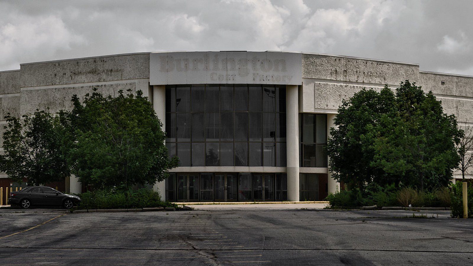 The exterior of an old abandoned mall and an empty parking lot.