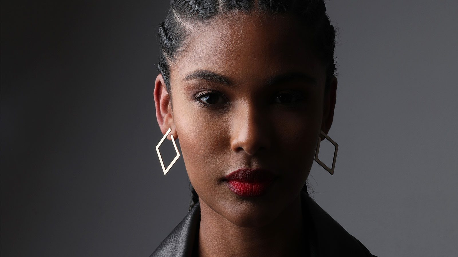 a photo of a pretty black woman with long cornrolls wearing a leather jacket.