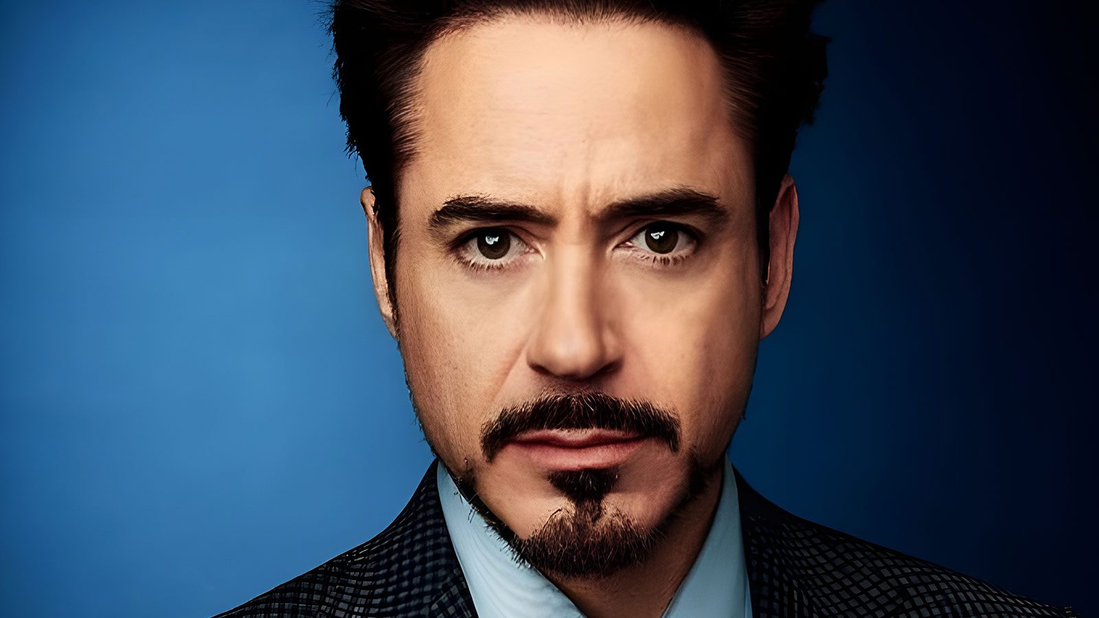 An image of Robert Downey Jr.- A white middle aged man with short brown hair, beard, and in a blue suit.