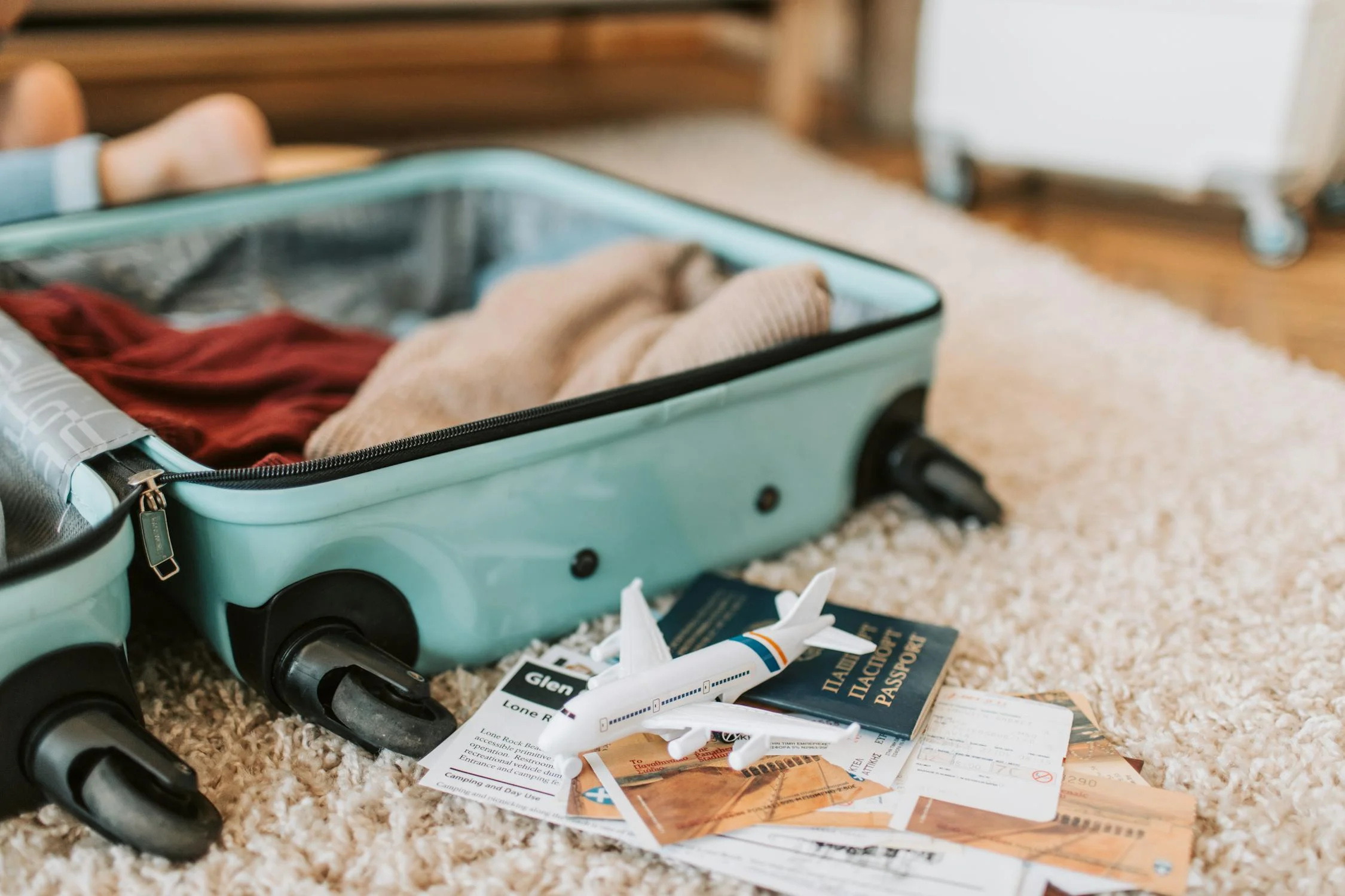pexels-photo-7368191 (1) an image of an open suitcase with half packed with clothes sitting on top of, a passport, and a map