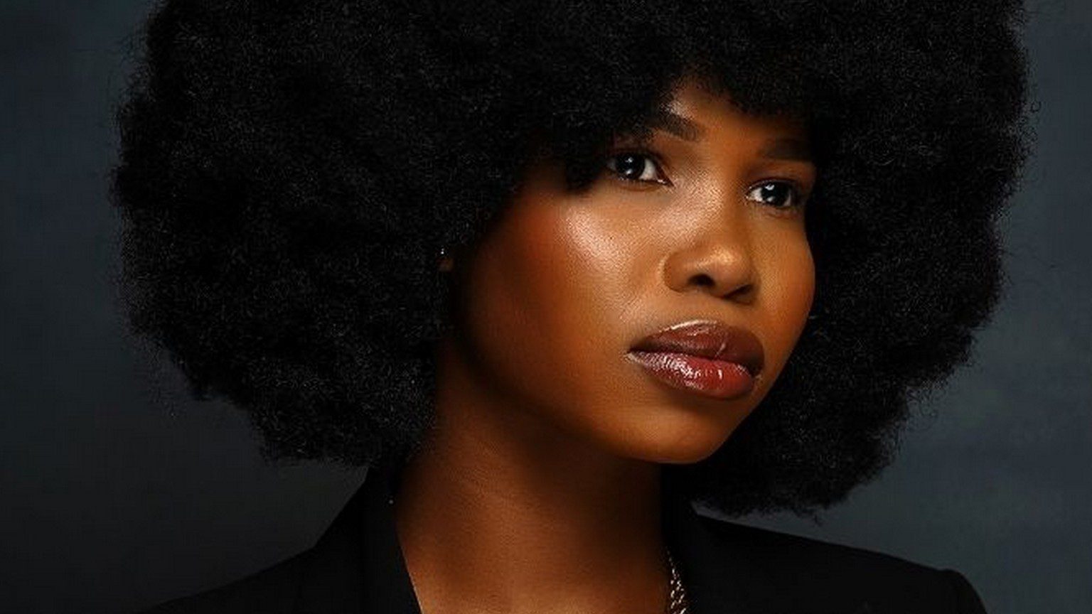A beautiful black woman with dark skin and a big afro dressed in a suit