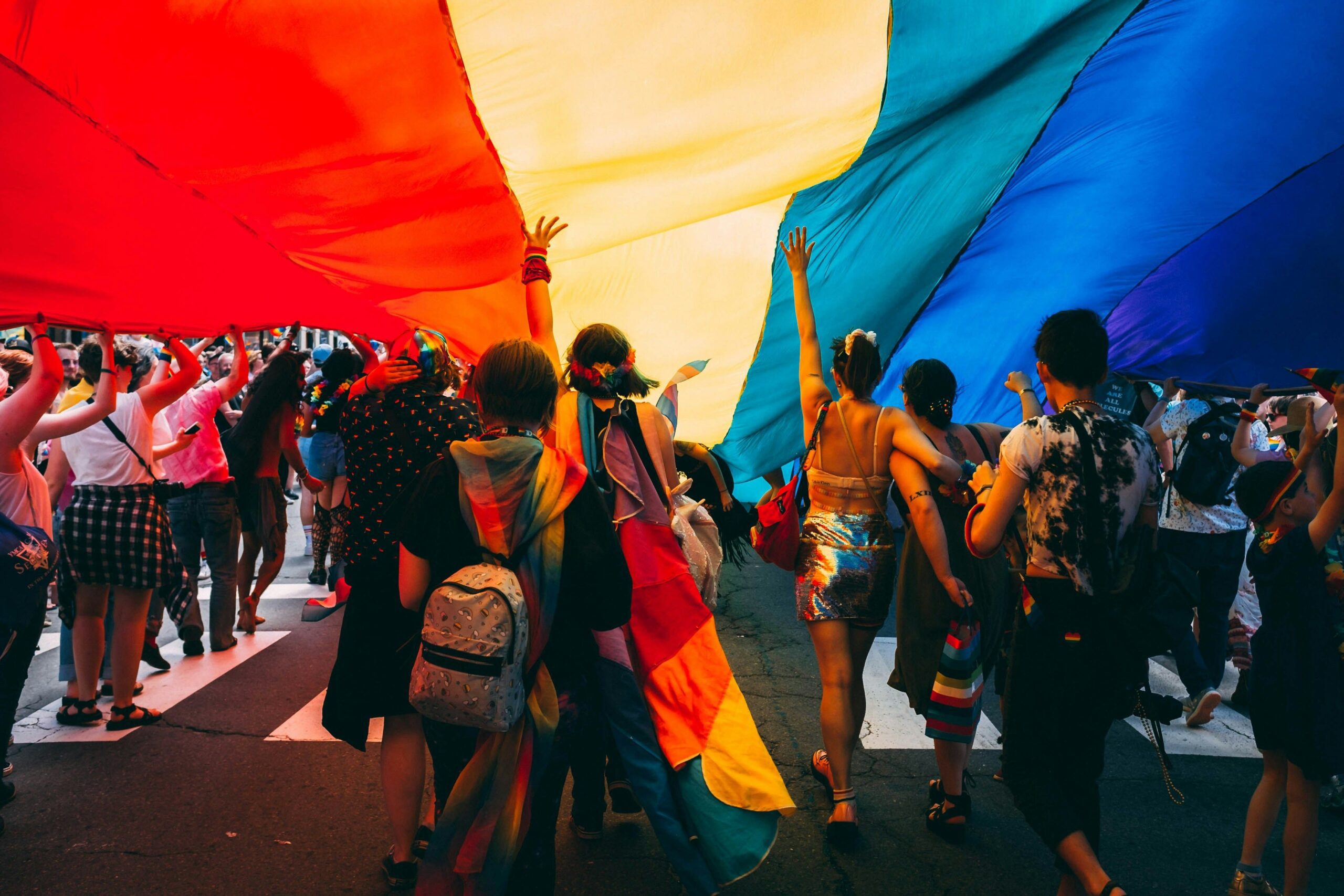 pride A group of people walking under a large pride flag during a pride parade