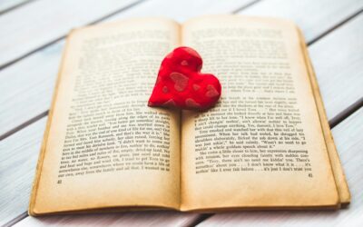 an image of an open book with a read plushie heart sitting on topping of the pages.