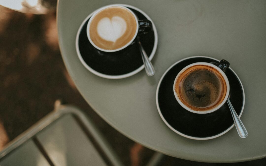 an image of two lattes in mugs on a table, one of the lattes is in the shape of a heart.