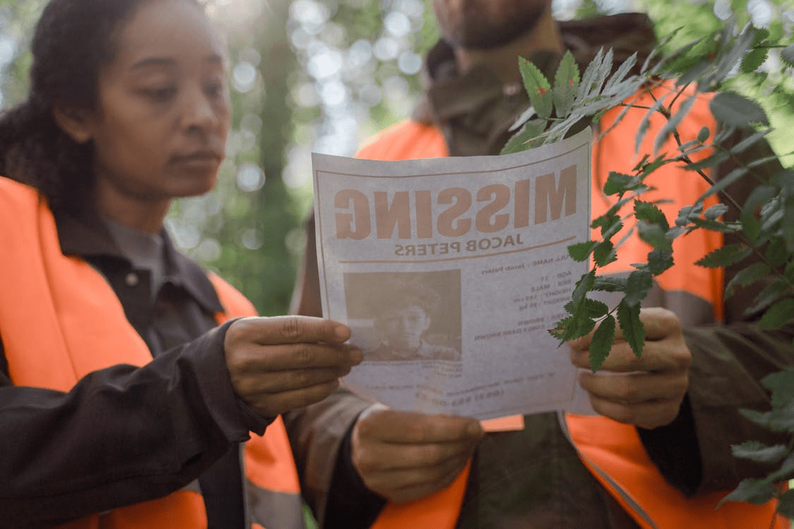 an image of a man and woman wearing orange safety vests holding up a missing person's poster. 