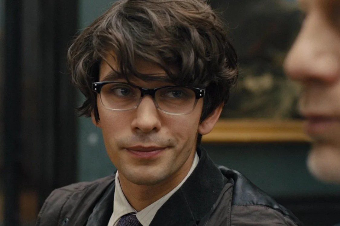 cat's out of the bag an image of ben whishaw from the skyfall movie. A young man with wavy brown hair, glasses, and dressed like a hipster.