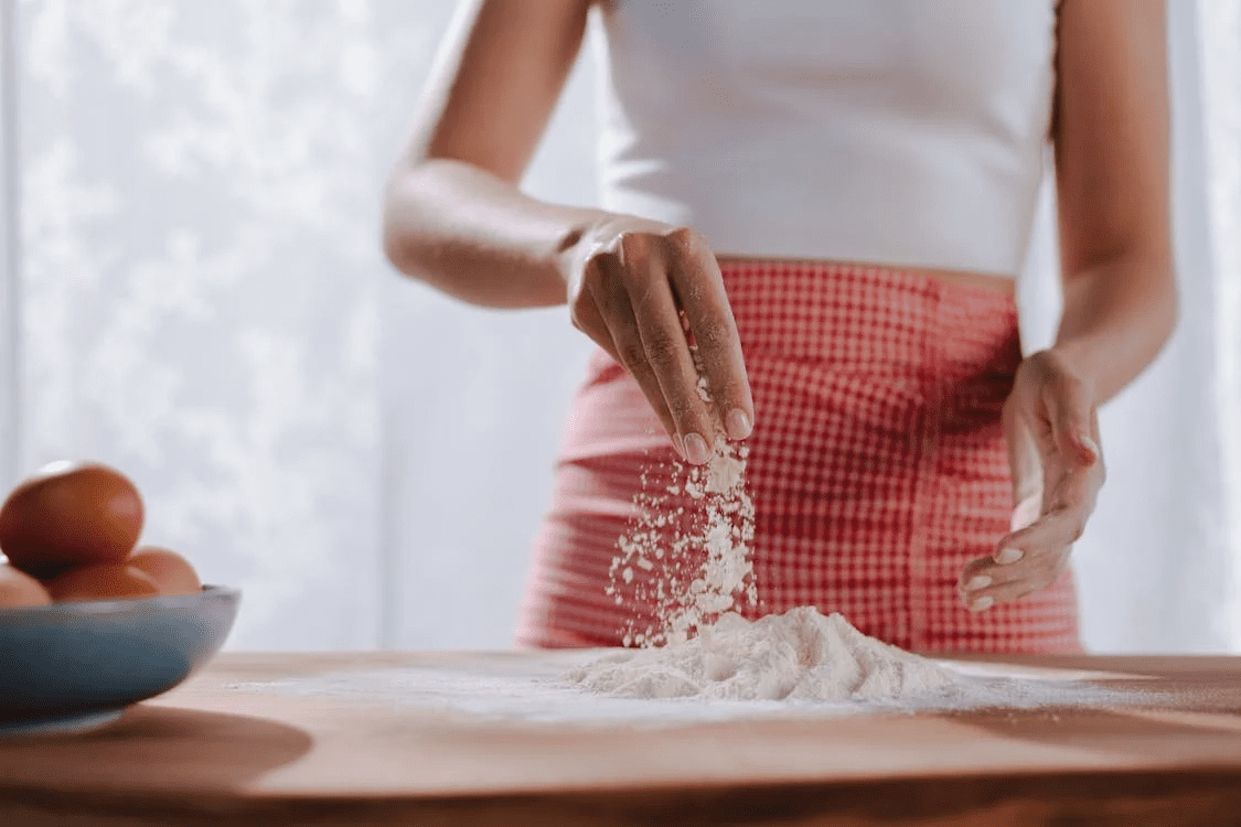 a woman using flour to bake something. 