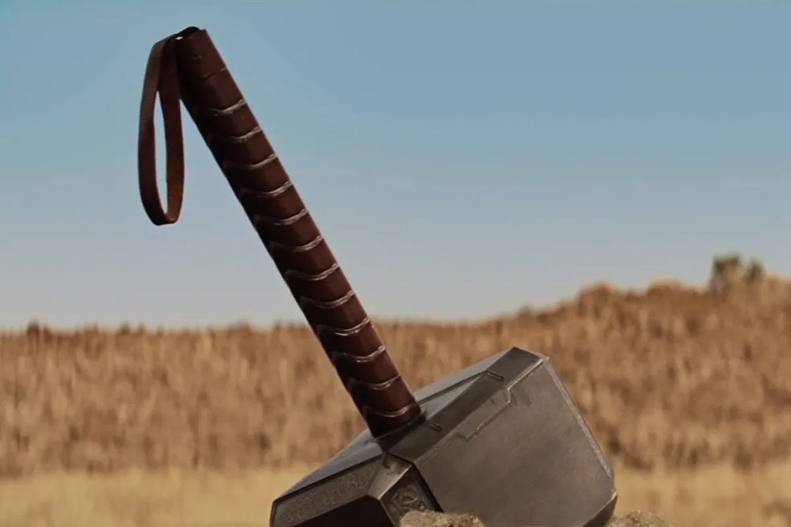 Close-up of a heavy metal hammer with a dark, wrapped handleClose-up of a heavy metal hammer with a dark, wrapped handle and looped end, resting in a dry field beneath a clear blue sky. 