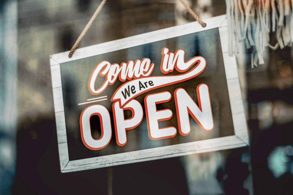 A hanging vintage shop sign reads “Come in, We Are OPEN” in bold red-and-white lettering.